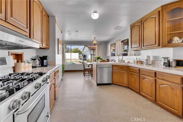 kitchen with baseboards, under cabinet range hood, appliances with stainless steel finishes, brown cabinetry, and a sink