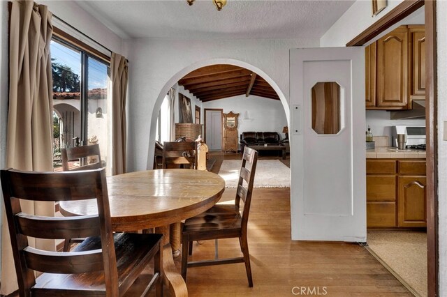 dining room with lofted ceiling, arched walkways, light wood finished floors, and a textured ceiling