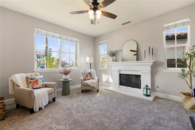 living area with visible vents, a ceiling fan, a glass covered fireplace, carpet floors, and baseboards