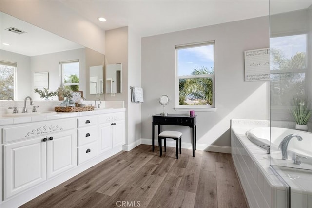 full bath featuring a sink, a healthy amount of sunlight, wood finished floors, and double vanity