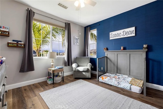 bedroom with a ceiling fan, wood finished floors, visible vents, and baseboards