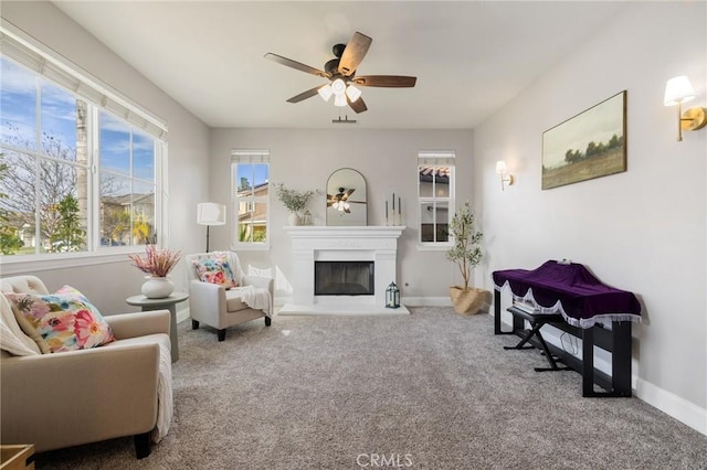 sitting room with carpet flooring, a ceiling fan, baseboards, and a glass covered fireplace