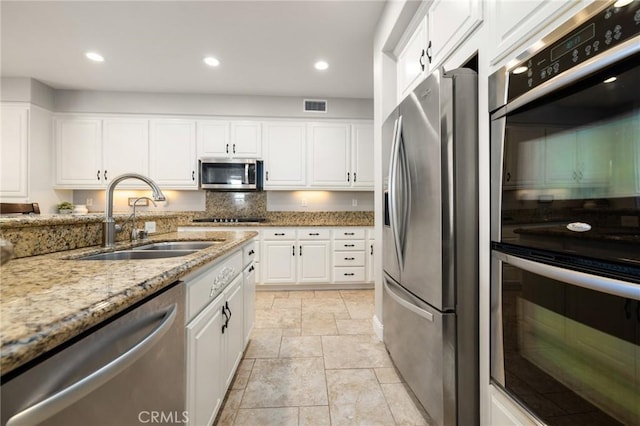 kitchen with light stone countertops, visible vents, a sink, appliances with stainless steel finishes, and white cabinetry