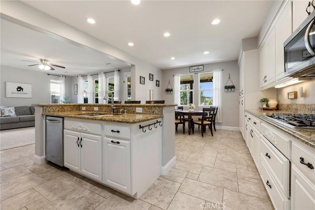 kitchen featuring recessed lighting, a sink, stainless steel appliances, white cabinets, and open floor plan