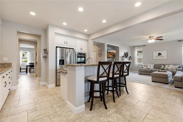 kitchen with light stone countertops, recessed lighting, a kitchen breakfast bar, white cabinets, and stainless steel appliances