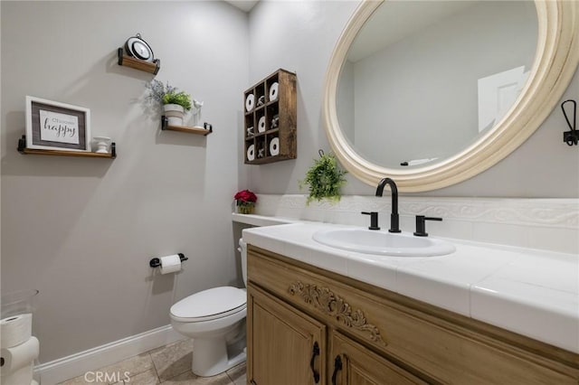 half bathroom with vanity, toilet, and baseboards