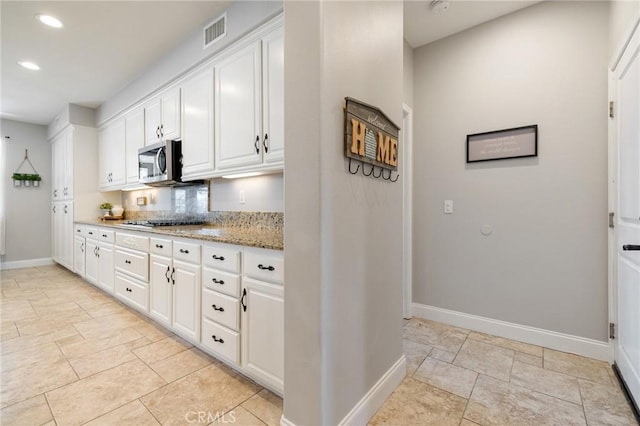 kitchen with stainless steel microwave, white cabinets, baseboards, and visible vents