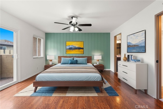 bedroom with wood finished floors, baseboards, ceiling fan, an accent wall, and access to outside