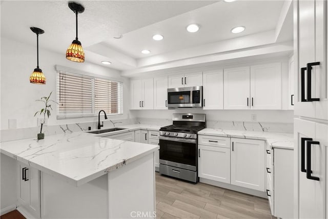 kitchen featuring a peninsula, a sink, stainless steel appliances, white cabinetry, and a raised ceiling