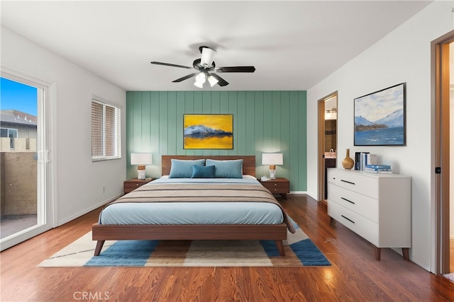 bedroom with a ceiling fan, wood finished floors, baseboards, access to exterior, and an accent wall