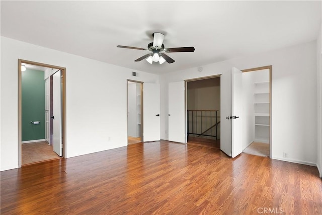 unfurnished bedroom featuring a ceiling fan, a spacious closet, wood finished floors, and a closet