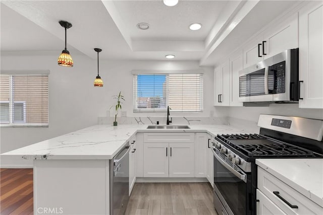 kitchen featuring a tray ceiling, light wood-style flooring, appliances with stainless steel finishes, a peninsula, and a sink