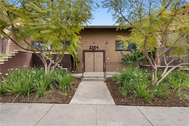 doorway to property with stucco siding and fence