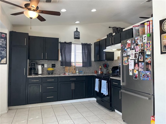 kitchen featuring black range with gas stovetop, backsplash, under cabinet range hood, freestanding refrigerator, and a sink