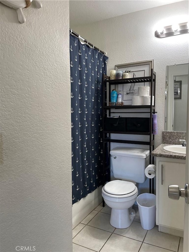 full bathroom with tile patterned floors, toilet, vanity, and a textured wall