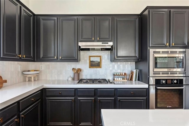 kitchen featuring under cabinet range hood, light countertops, tasteful backsplash, and appliances with stainless steel finishes