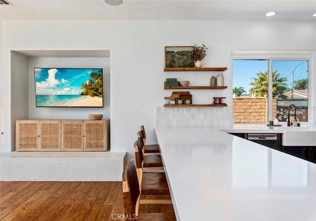 interior space featuring open shelves, dishwasher, light countertops, wood finished floors, and a sink