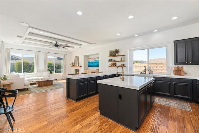 kitchen featuring dark cabinets, open floor plan, a kitchen island with sink, and light countertops