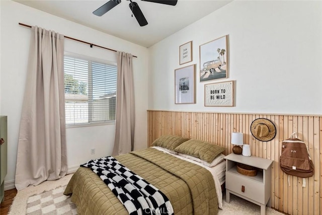 bedroom with wainscoting, wood walls, and ceiling fan