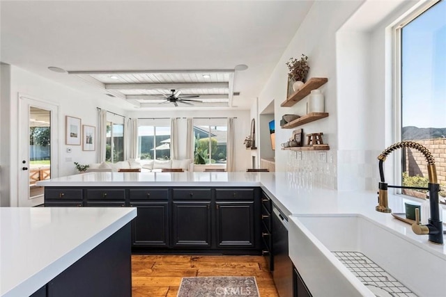 kitchen featuring a sink, dark cabinetry, light wood-style floors, a peninsula, and light countertops