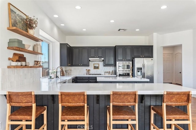 kitchen with visible vents, backsplash, under cabinet range hood, light countertops, and appliances with stainless steel finishes