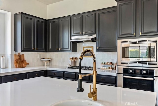 kitchen featuring under cabinet range hood, appliances with stainless steel finishes, tasteful backsplash, and light countertops