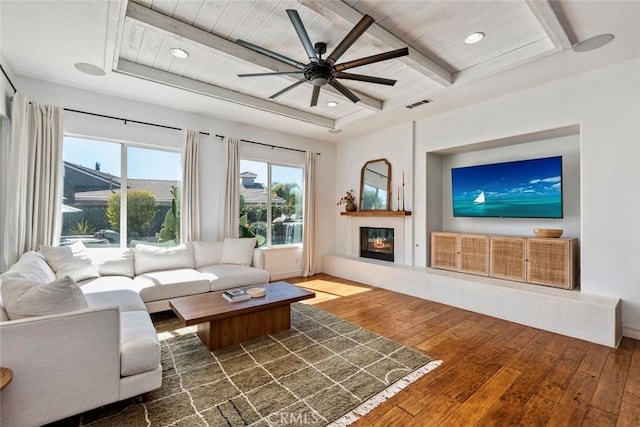 living area with beamed ceiling, visible vents, a glass covered fireplace, recessed lighting, and wood-type flooring