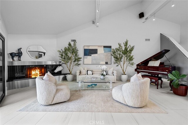 living area with lofted ceiling with beams, visible vents, a warm lit fireplace, and track lighting