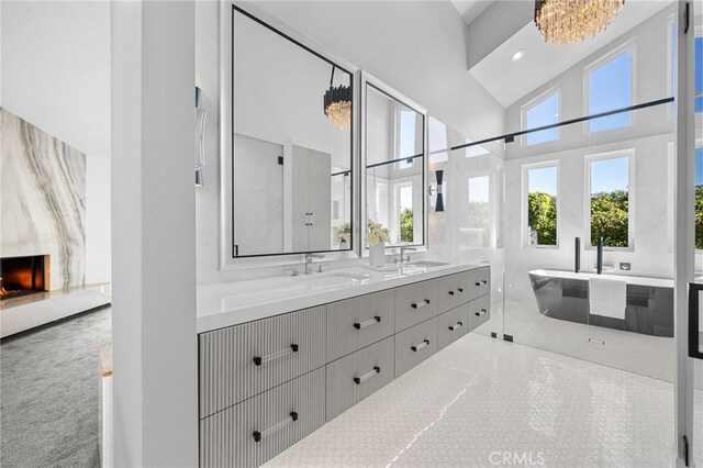 full bathroom featuring double vanity, a premium fireplace, a towering ceiling, a freestanding tub, and a sink