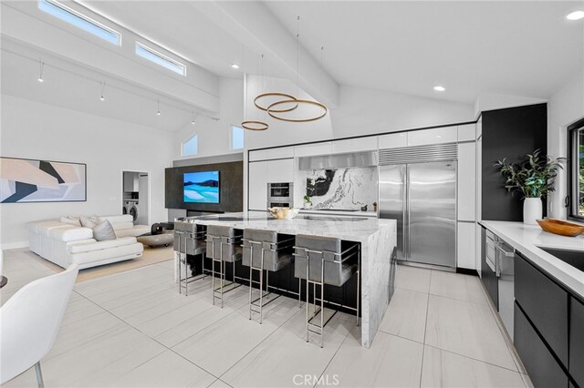 kitchen with a kitchen bar, built in fridge, hanging light fixtures, high vaulted ceiling, and modern cabinets