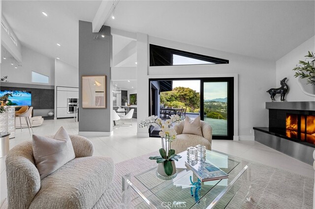 living room featuring light tile patterned flooring, baseboards, a warm lit fireplace, and high vaulted ceiling