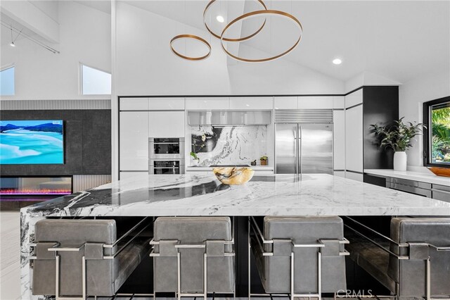 kitchen featuring a large island, stainless steel appliances, light stone countertops, and high vaulted ceiling