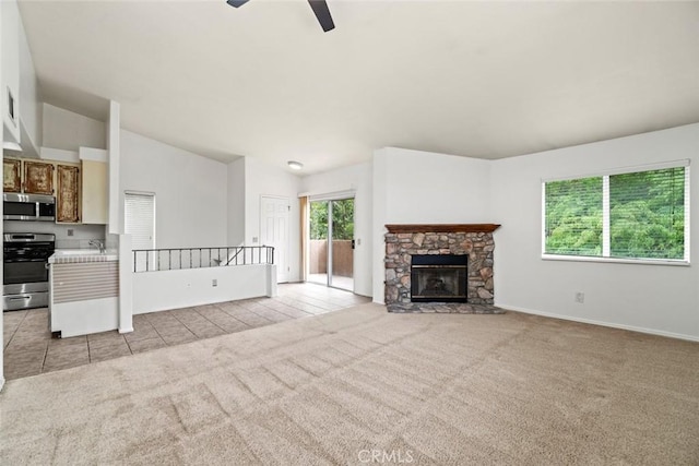 unfurnished living room featuring lofted ceiling, light carpet, a stone fireplace, light tile patterned flooring, and a ceiling fan