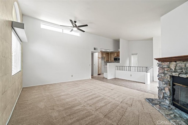 unfurnished living room featuring a stone fireplace, light colored carpet, visible vents, and ceiling fan