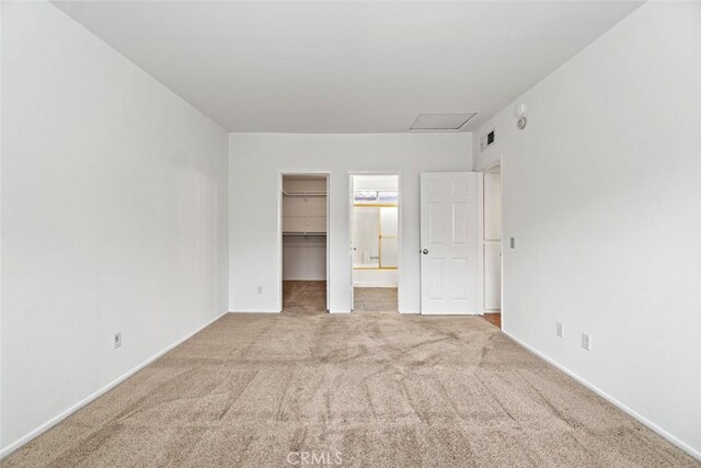 unfurnished bedroom with visible vents, a walk in closet, attic access, carpet flooring, and a closet