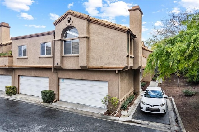 view of front of home featuring a tile roof, stucco siding, an attached garage, and a chimney