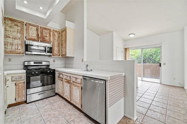 kitchen with a sink, a peninsula, appliances with stainless steel finishes, and tile counters