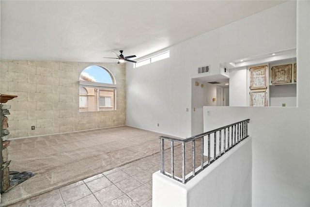 tiled spare room with carpet flooring, a ceiling fan, a high ceiling, and visible vents