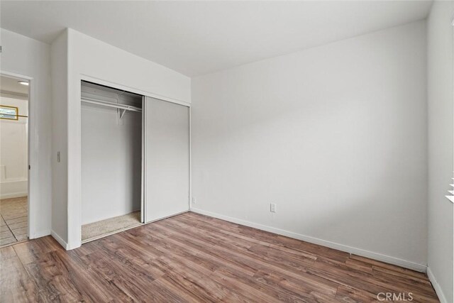 unfurnished bedroom featuring a closet, baseboards, and wood finished floors