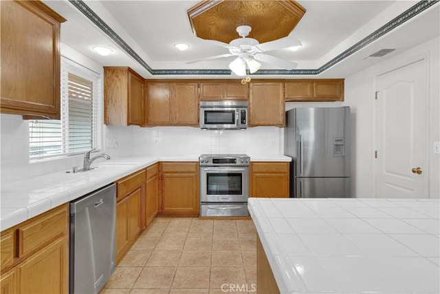 kitchen with a tray ceiling, light tile patterned floors, a sink, tile countertops, and appliances with stainless steel finishes