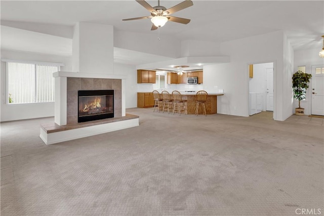 unfurnished living room with light carpet, vaulted ceiling, a tiled fireplace, and a ceiling fan