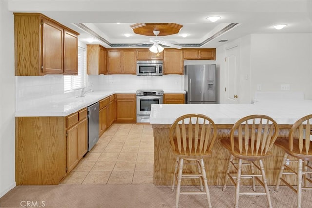 kitchen featuring a tray ceiling, a kitchen bar, stainless steel appliances, and a peninsula