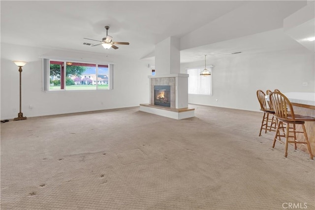 unfurnished living room featuring light colored carpet, ceiling fan, a tile fireplace, and a wealth of natural light