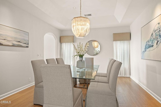 dining space with arched walkways, visible vents, baseboards, and wood finished floors