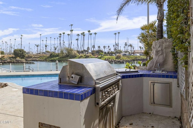 view of patio with a water view, exterior kitchen, area for grilling, an outdoor pool, and a sink