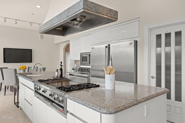 kitchen featuring a kitchen island, arched walkways, stone countertops, stainless steel appliances, and a sink