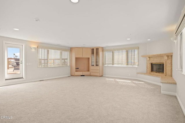 unfurnished living room with a high end fireplace, light colored carpet, a wealth of natural light, and baseboards