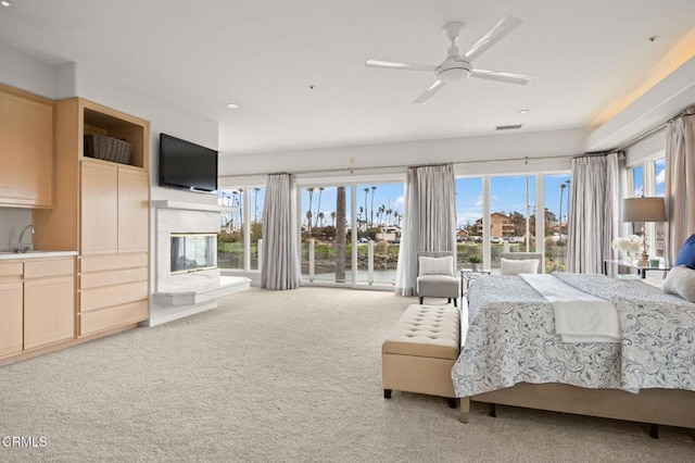 carpeted bedroom with a glass covered fireplace, multiple windows, visible vents, and a sink