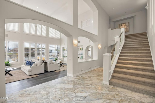 foyer entrance with stairway, baseboards, a high ceiling, arched walkways, and marble finish floor