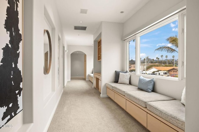 corridor featuring baseboards, visible vents, arched walkways, and light carpet